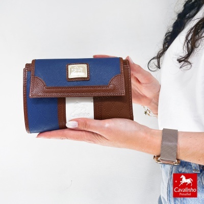 Carteira Cavalinho azul e castanha com placa metálica dourada segurada por pessoa