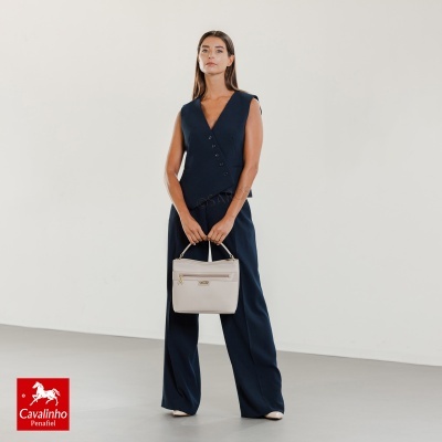 Mulher com colete e calças azuis a segurar mala bege clara