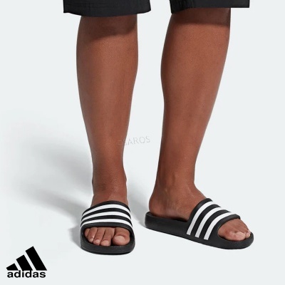 Chinelos Adidas pretos com riscas brancas em pessoa