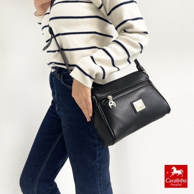 Mala preta em pele com pendente e alça ajustável a uma modelo vestida de camisola às riscas e jeans