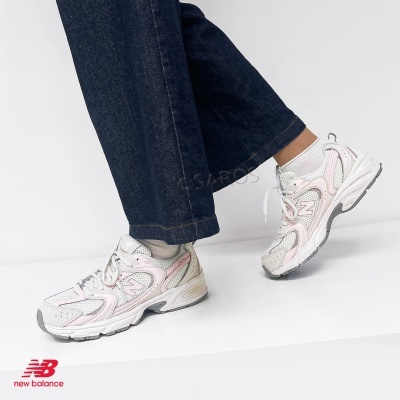 Ténis New Balance brancos com montagem rosa e cinza, usados com meias brancas e calças de ganga azul escuro