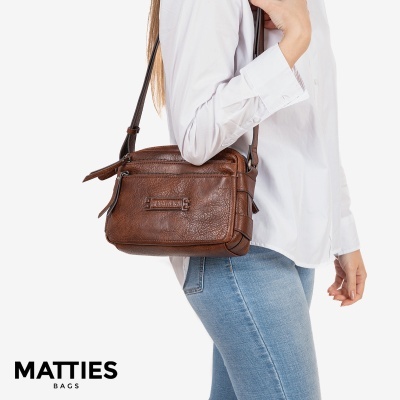 Mala castanha em pele com alça ao ombro em modelo vestindo camisa branca e jeans azuis