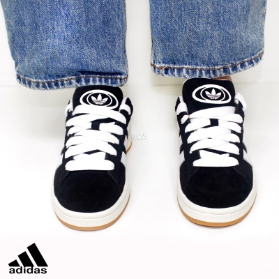 Ténis Adidas pretos com sola branca e cordões brancos usados com calças de ganga azul