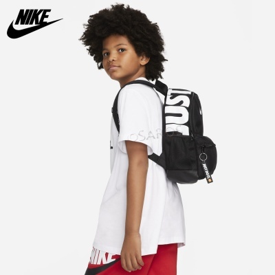 Mochila preta Nike com texto branco, usada por garoto de camiseta branca e calças vermelhas