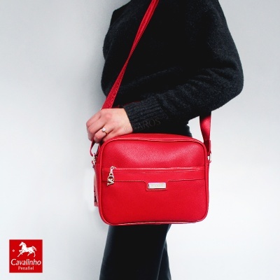 Mala vermelha de tiracolo com pendente e bolso frontal, usada por pessoa com roupa preta