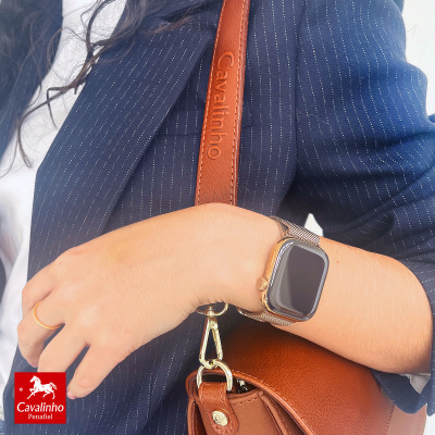 Bolsa de pele castanha com alça Cavalinho e pessoa com blazer azul e relógio digital