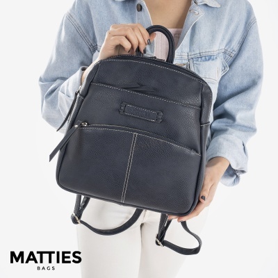 Mochila preta em pele sintética com fecho e costuras brancas segurada por pessoa com casaco de ganga.