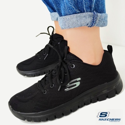 Ténis pretos Skechers com logo cinza, usados com jeans azuis dobrados