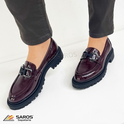 Sapatos mocassim castanhos em verniz com sola preta e fivela metálica, usados com calças pretas.