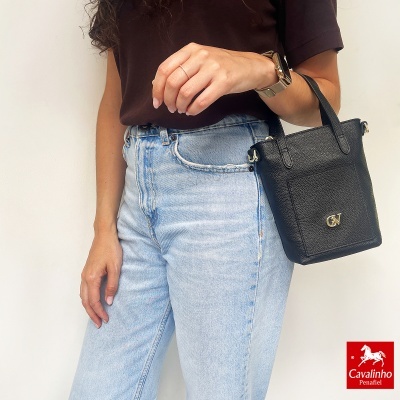 Mala preta de pele com textura granulado com logo CV e alças ao lado de jeans azul claro