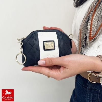 Carteira pequena preta e branca com etiqueta dourada Cavalinho, sendo segurada por uma mão feminina