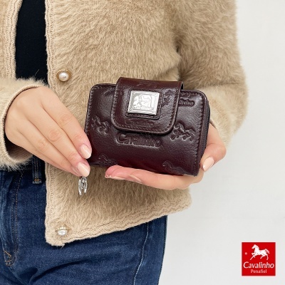 Carteira castanha de pele com padrão de cavalos e placa metálica, segurada por pessoa com casaco bege