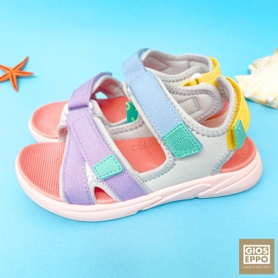 Sandálias infantis coloridas com tiras lilás, azul claro e amarelo, palmilha rosa e sola branca sobre fundo azul com conchas e estrela-do-mar.