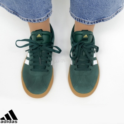 Tênis Adidas verde escuro com sola castanha clara usados por pessoa com calças de ganga azuis