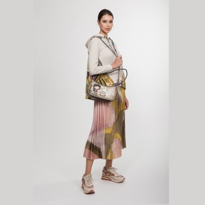 Mulher com mala bege estampada, camisola bege com capuz, saia plissada rosa, verde e amarelo e sapatilhas bege com detalhes coloridos