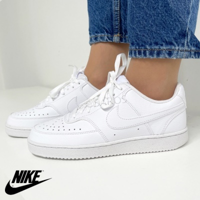 Sapatilhas brancas Nike com detalhes perfurados, usadas com calças de ganga