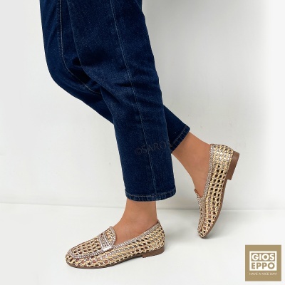 Sapatos mocassim dourados trançados com calças de ganga azul e fundo branco