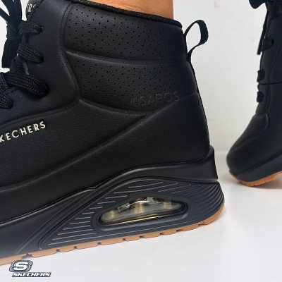 Ténis Skechers pretos com sola preta e detalhes em borracha caramelo, com amortecimento visível na sola.