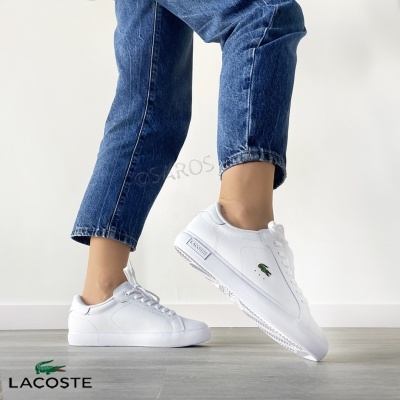 Ténis brancos Lacoste com logótipo verde usados com jeans azuis