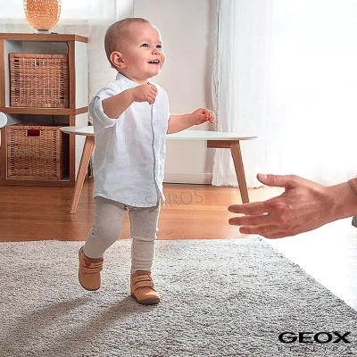 Bebé a andar em tapete cinzento com sapatos camel e mapa GEOX no canto