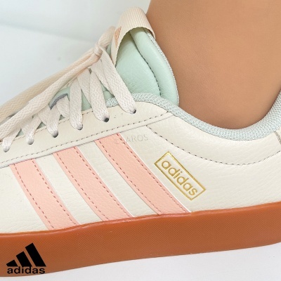 Tênis Adidas branco com riscas rosa e sola castanha em fundo branco