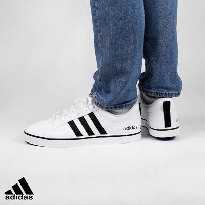 Ténis Adidas brancos com riscas pretas usados com jeans azuis.