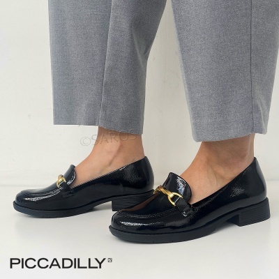 Sapatos mocassim pretos em verniz com fivela dourada usados por pessoa com calças cinzentas