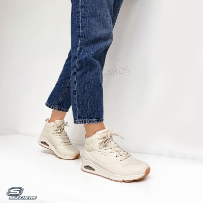 Ténis Skechers bege claro usados com jeans azuis sobre fundo branco