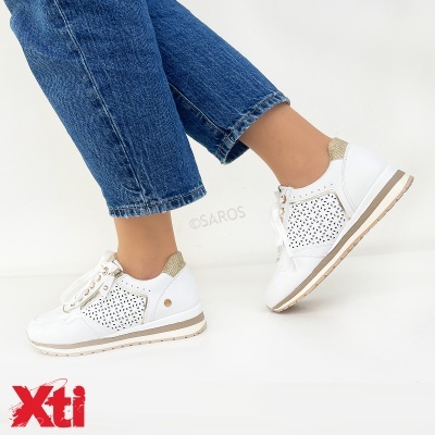 Tênis branco com detalhes dourados e sola branca usados com jeans azul.