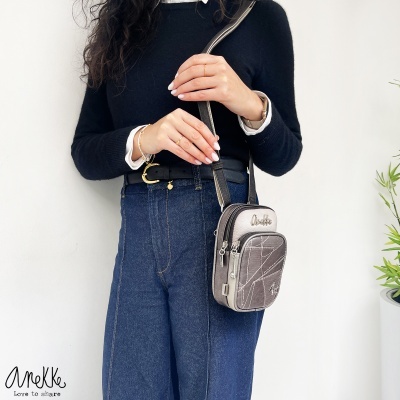 Mala pequena cinza e bege com texto Anekke usada por mulher com camisola preta e calças de ganga