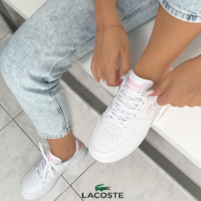 Ténis brancos Lacoste com detalhes rosas usados por pessoa com jeans claros