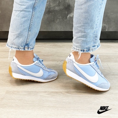 Ténis Nike azuis e cinza com sola castanha usados com calças azuis claras