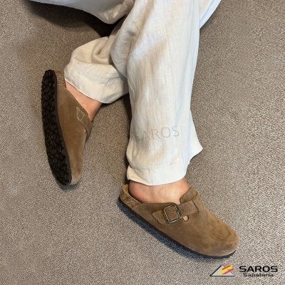 Sapatos mule castanhos em camurça com fivela em pessoa com calças bege em carpete castanha.