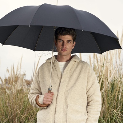 Homem com casaco bege felpudo a segurar um guarda-chuva preto com pega de madeira