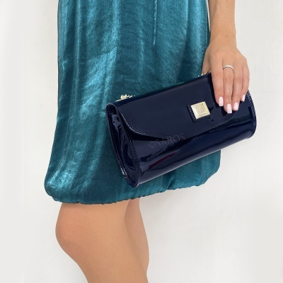 Mala de mão azul escuro verniz segurada por mulher com vestido azul esverdeado