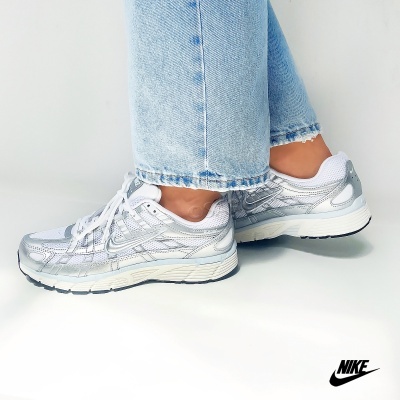 Ténis Nike brancos e cinza prateado usados com jeans azuis