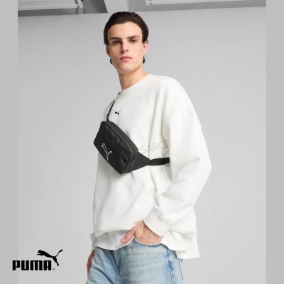 Pessoa com mochila preta Puma passada transversalmente sobre túnica branca e calças de ganga azuis claras