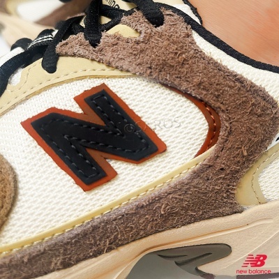 Tênis New Balance branco com camurça castanha e selo N preto com contorno vermelho