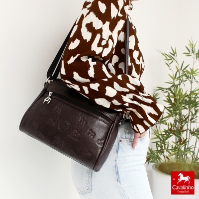 Mala castanha em pele com relevos e fecho metálico usada com camisa estampada e jeans