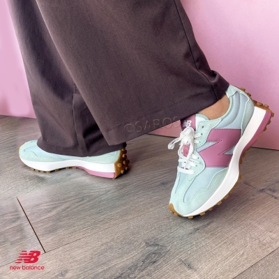 Sapatilhas New Balance azul claro e rosa com sola castanha, calças castanhas, fundo rosa