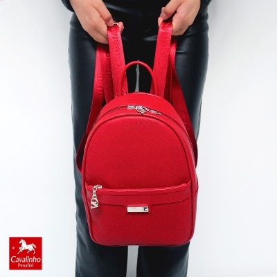 Mochila pequena vermelha com alças largas sendo segurada por uma pessoa.