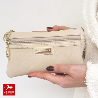 Carteira pequena bege com detalhes dourados e logo Cavalinho nas mãos de uma pessoa