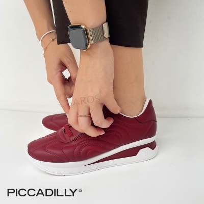 Ténis vinho com sola branca da marca PICCADILLY usados por uma pessoa com relógio dourado e pulseiras, fundo branco