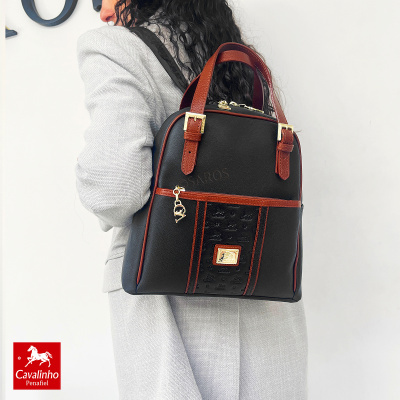 Mochila preta com detalhes castanhos e fecho dourado, usada por pessoa com casaco cinzento