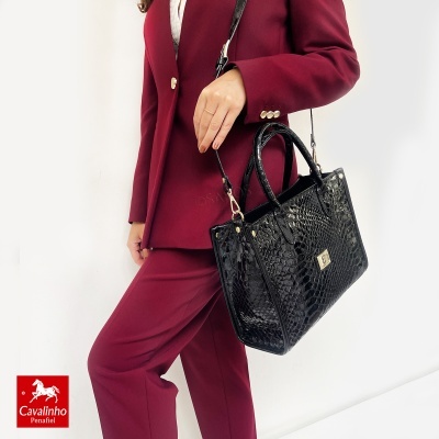 Mala preta padrão pele de crocodilo com fecho dourado e alças, combinada com fato borgonha feminino