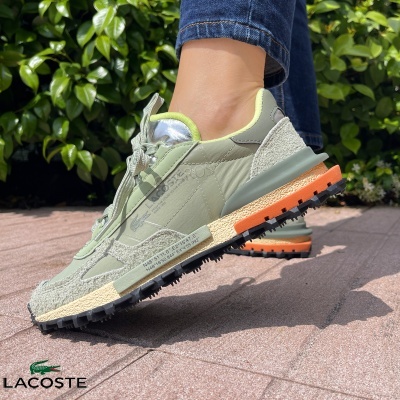 Ténis Lacoste verde pastel e laranja com sola preta e detalhes em camurça, usados ao ar livre