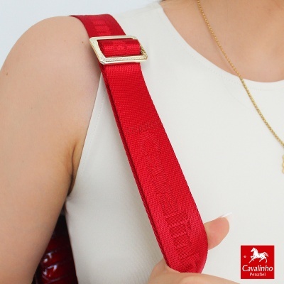 Alça de bolsa vermelha com fivela dourada em ombro de pessoa com blusa branca