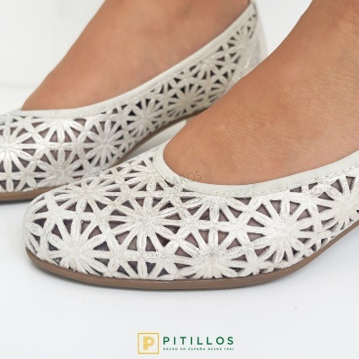 Sapatilhas brancas com padrão recortado em estrelas e flores, sola castanha.