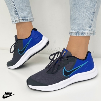 Ténis Nike cinzento escuro e azul com sola branca usados com calças de ganga claras