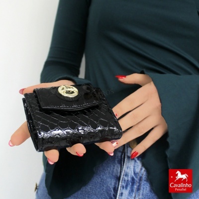 Carteira preta pequena com textura de pele de crocodilo e fecho prateado, em mãos femininas com unhas vermelhas